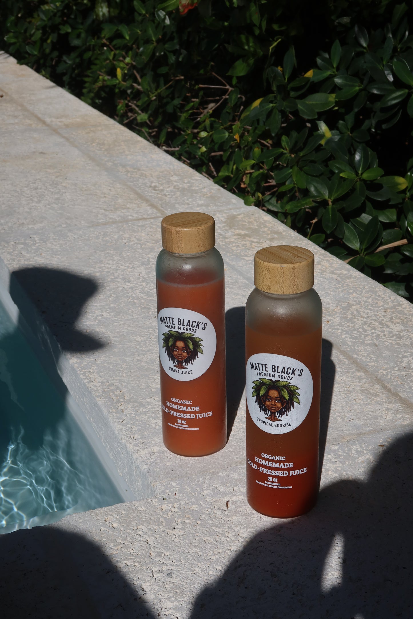 Two bottles of Matte Black's juice on a stone surface with a pool in the background.